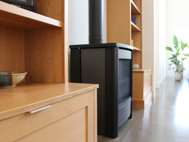 Close up of natural wood builtin cabinets with a black iron, wood burning stove on a polished concrete floor